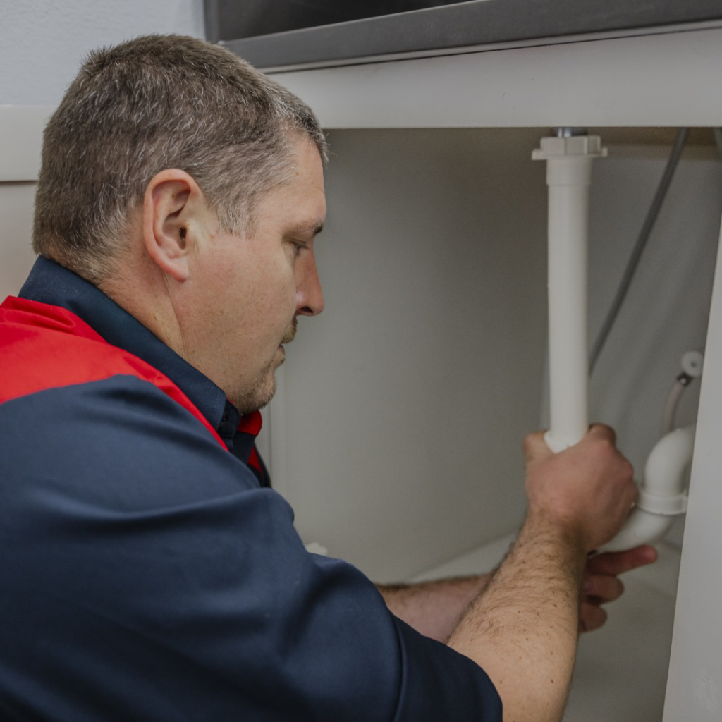 A Service Squad Plumbing technician working on pipes under a kitchen sink in Fort Worth, TX.