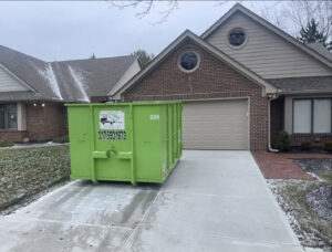 A Bin There Dump That green dumpster on a residential driveway during winter, providing junk removal services in Indianapolis, IN.