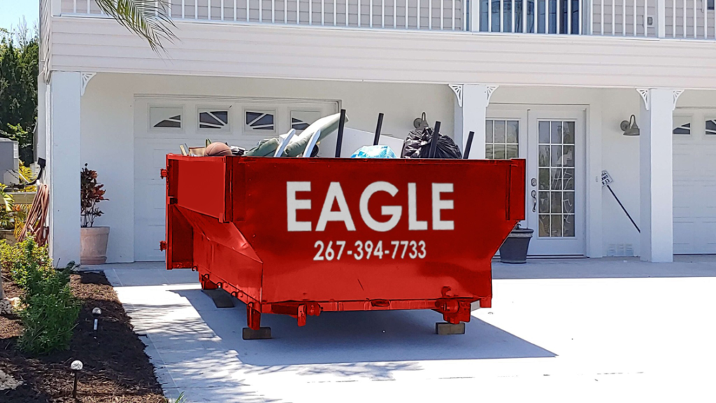 A red dumpster filled with household junk placed in a residential driveway by Eagle Dumpster Rental in Philadelphia, PA.