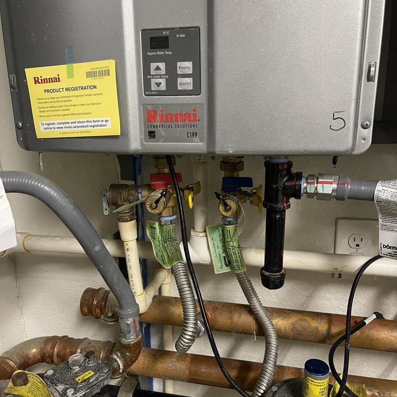 A Rinnai tankless water heater unit with control panel and plumbing connections, serviced by Tribeca Plumbing in Dallas, TX.