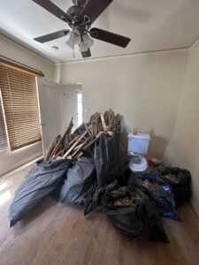 A room filled with black trash bags and wooden debris, awaiting junk removal by Crisan Junk Removal in San Diego, CA.