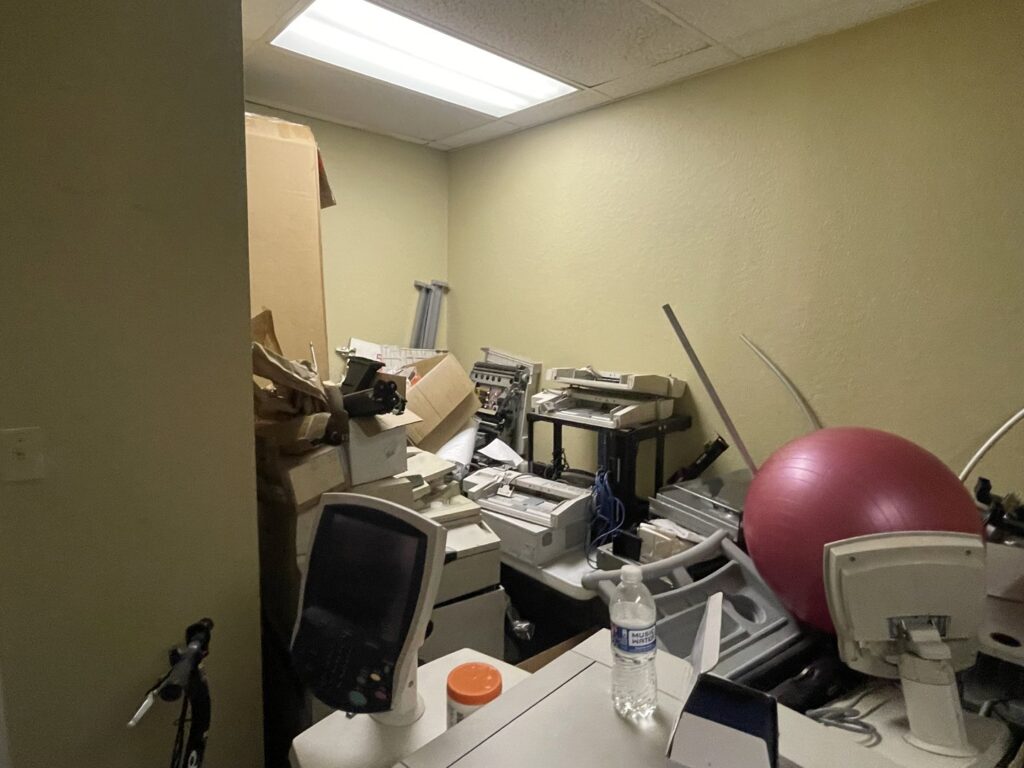 A room filled with old office equipment, printers, and boxes, needing junk removal services from Duane's junk removal LLC in Houston, TX.