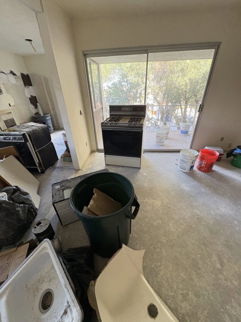 An indoor scene showing a room piled high with wood, sinks, and various debris, indicating a junk removal job by Priority Hauling and Junk Removal San Diego.