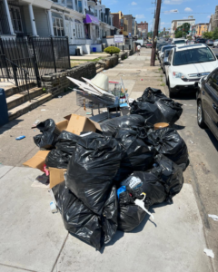 A large pile of black trash bags and cardboard boxes on a sidewalk, awaiting junk removal by JUNK BOX LLC in Philadelphia, PA.