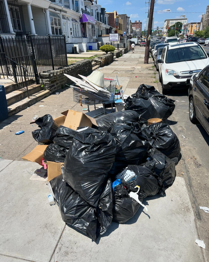 A large pile of black trash bags and cardboard boxes on a sidewalk, awaiting junk removal by JUNK BOX LLC in Philadelphia, PA.
