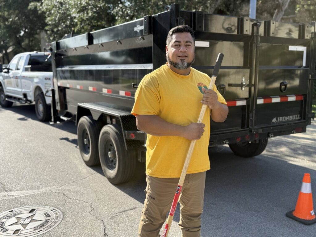 A Silverhull Junk Removal employee in a branded shirt standing proudly in front of a dump trailer in San Antonio, TX.