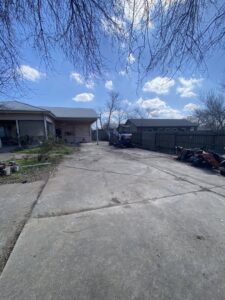 A site clearing job in progress with an excavator and debris piles on a concrete driveway by JT Junk Solutions in Austin, TX.
