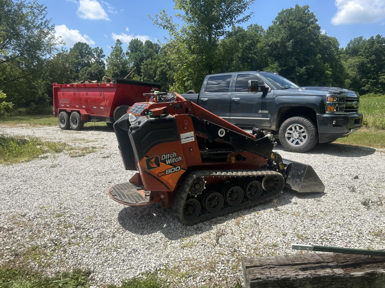 A Ditch Witch skid steer and a pickup truck with a red dump trailer full of debris, used by Z & Z Services in Indianapolis, IN.