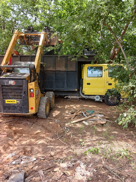 A skid steer loading various junk and debris into a large truck for DonkeyJunk Removal and Home Services in Austin, TX