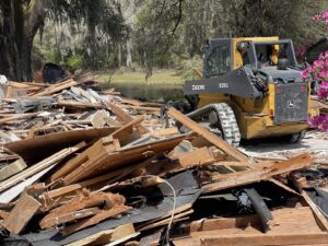 A skid steer loader next to a large pile of wood and construction debris, indicating a heavy-duty junk removal job by Jacksonville Hauling & Junk Removal in Jacksonville, FL.