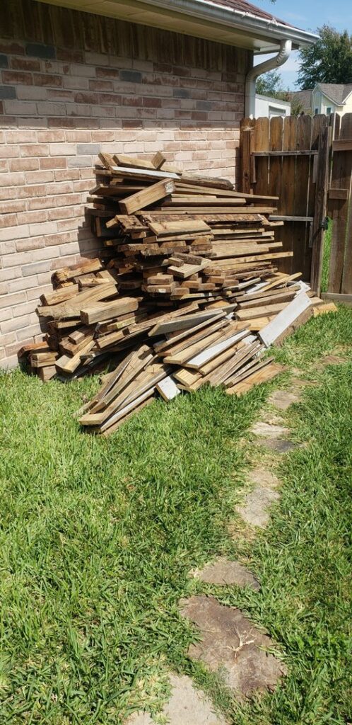 A neatly stacked pile of wood planks and debris in a backyard, ready for junk removal by Duane's junk removal LLC in Houston, TX.