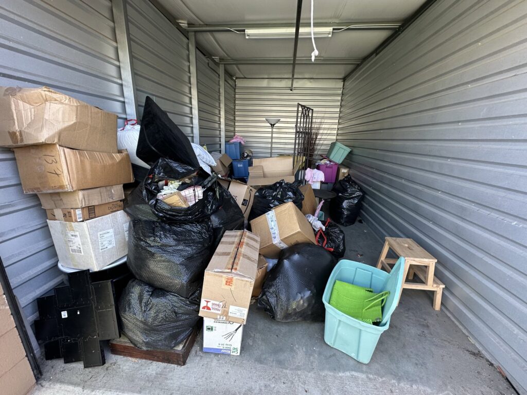 A cluttered storage unit filled with boxes and trash, indicating a cleanout job by Haul Away Any Day in San Diego, CA.