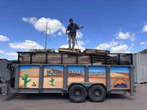 A North Valley Junk Removal team member loading wooden pallets onto a branded trailer during a junk removal job in Phoenix, AZ.