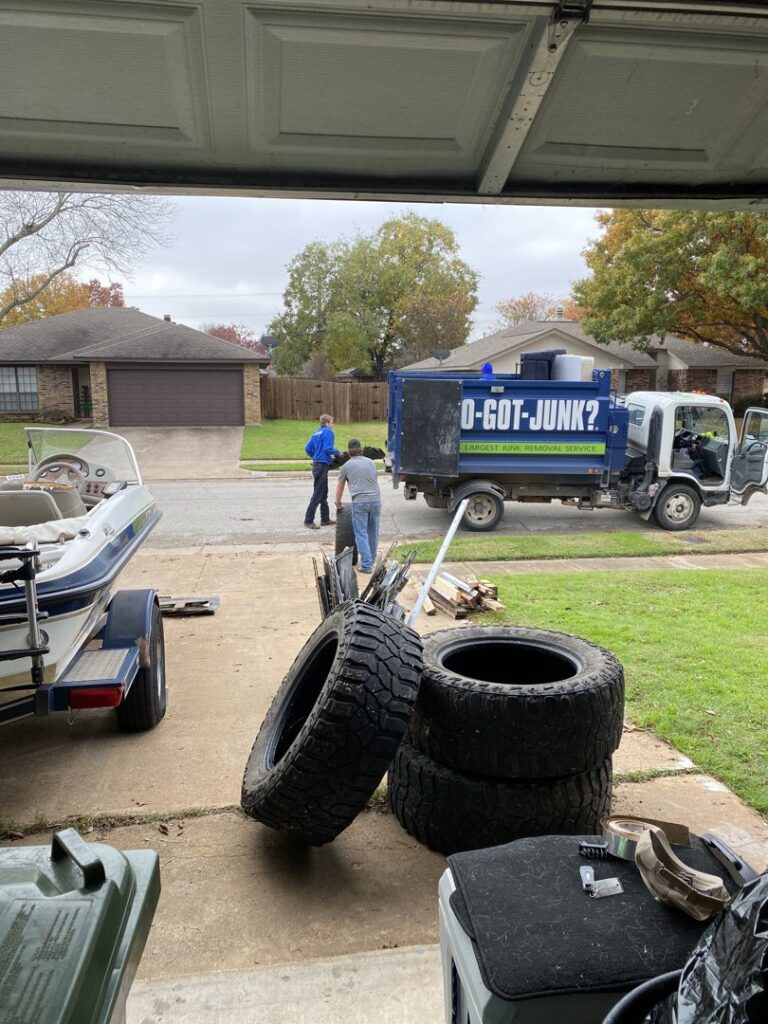 A pile of old tires and debris in a garage, with 1-800-GOT-JUNK? crew and truck ready for removal in Fort Worth, TX.