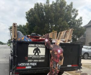 A trailer loaded with various junk items, including pallets and bags, with an Iron Man cutout, by Controlled Chaos Services in San Antonio, TX