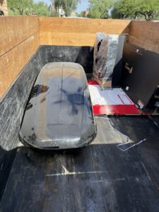 A Minutemen Junk Removal trailer loaded with a roof cargo box and other boxed items for disposal in Phoenix, AZ.