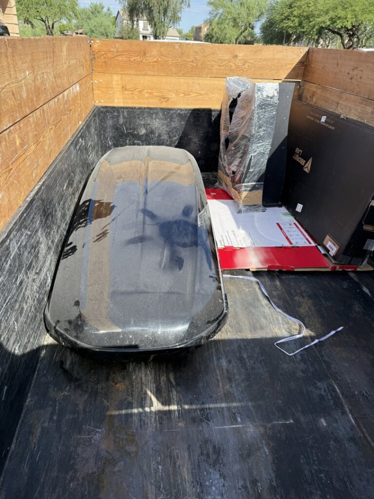 A Minutemen Junk Removal trailer loaded with a roof cargo box and other boxed items for disposal in Phoenix, AZ.