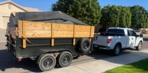 A Minutemen Junk Removal truck and trailer loaded with items, covered by a tarp, ready for disposal in Phoenix, AZ.