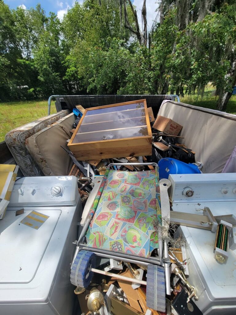 A junk removal truck bed filled with various household items like mattresses and appliances by The Mess Haul in Jacksonville, FL.