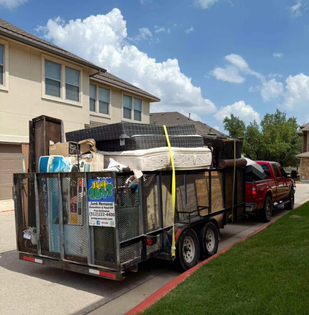 A JunkGuys Austin Junk Removal truck pulls a large trailer overflowing with mattresses, furniture, and various junk items in Austin, TX.