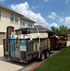 A JunkGuys Austin Junk Removal truck pulls a large trailer overflowing with mattresses, furniture, and various junk items in Austin, TX.