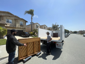 Two Republic Junk Removal workers loading a large wooden furniture piece onto a truck in San Diego, CA