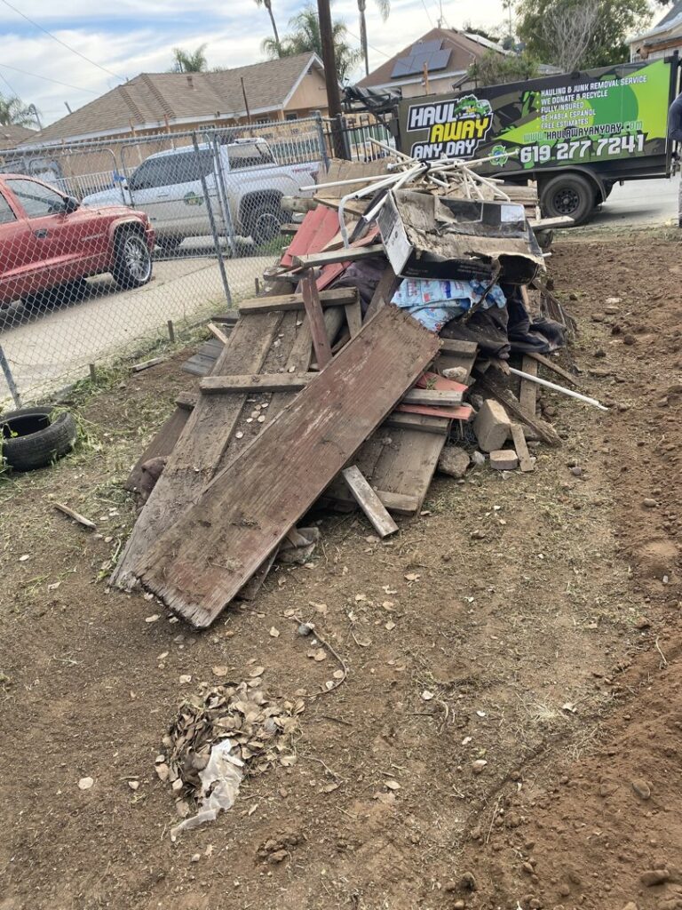 A pile of wood and construction debris on a dirt patch, ready for removal by Haul Away Any Day in San Diego, CA.