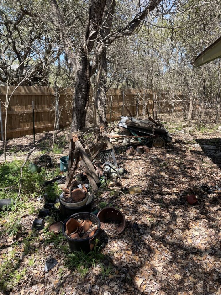 A wooded backyard area with piles of old pots, metal, and various debris ready for Firefighter Junk Removal in Austin, TX.