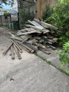 A large pile of wooden planks and debris on a concrete path, ready for removal by HustleTown Junk Removal in Houston, TX.