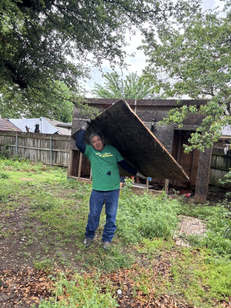 A Green Source Junk Removal worker carrying a large piece of debris from a demolished shed in Fort Worth, TX.