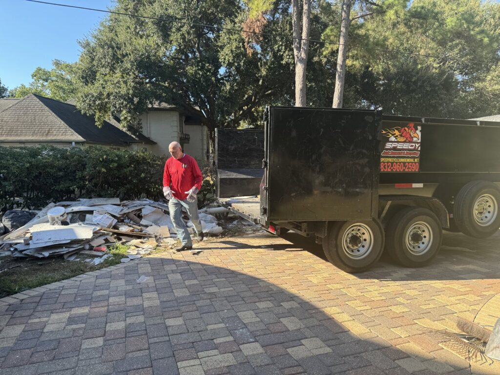 A Speedy Junk Removal & recycling worker clearing a large pile of debris from a driveway in Houston, TX.