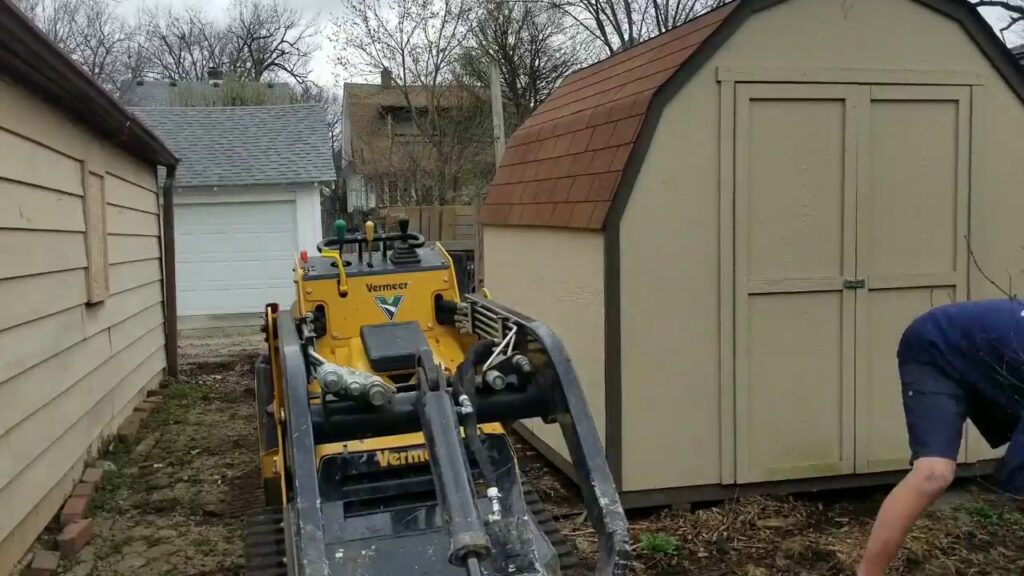A worker from Schott Services clearing debris next to a shed using a skid steer in Indianapolis, IN.