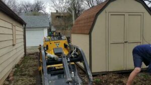 A worker from Schott Services clearing debris next to a shed using a skid steer in Indianapolis, IN.