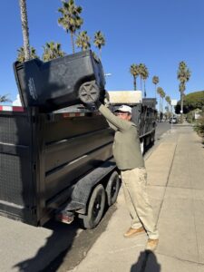 A worker from Fred's Junk Removal emptying a large trash bin into a junk removal trailer in Chula Vista, CA.