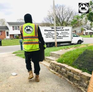 A worker from We Haul It Cleaning Service LLC in Canal Winchester, OH, hauling a trash can to their junk removal truck.