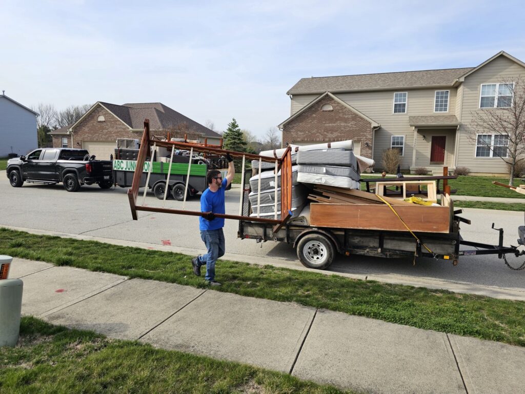 A worker loading a bed frame onto a junk removal trailer for ABC Junk Removal & Hauling in Westfield, IN.