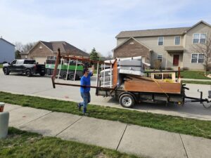 A worker loading a bed frame onto a junk removal trailer for ABC Junk Removal & Hauling in Westfield, IN.