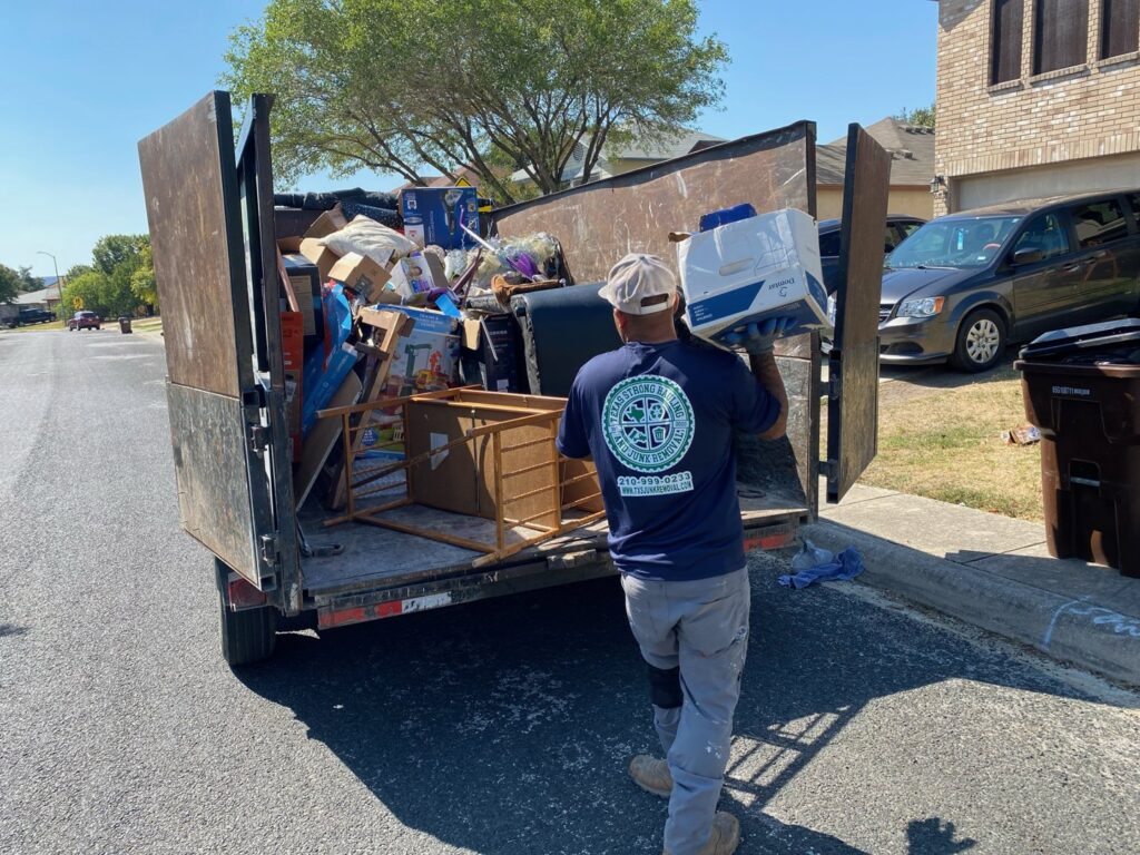 A worker loading a box into a full junk removal trailer for Texas Strong Hauling and Junk Removal in San Antonio, TX.