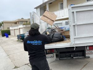 A Republic Junk Removal worker loading cardboard boxes into a truck filled with various junk in San Diego, CA