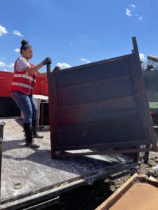 A worker from 2 Women with a Pickup Truck and Trailer Too LLC loading a dark wooden headboard into a dump trailer for junk removal in Columbus, OH.
