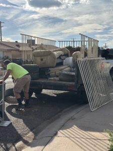 A worker loading old furniture and tires onto a junk removal trailer for J & R Junk Removal services in Phoenix, AZ.
