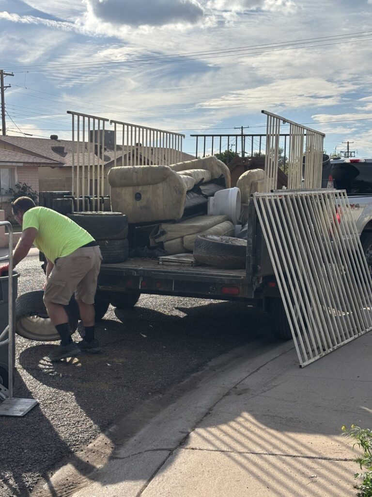 A worker loading old furniture and tires onto a junk removal trailer for J & R Junk Removal services in Phoenix, AZ.