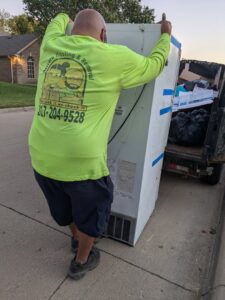 A worker from Herrera Hauling & Junk Removal loading a large appliance onto a trailer in Fort Worth, TX.
