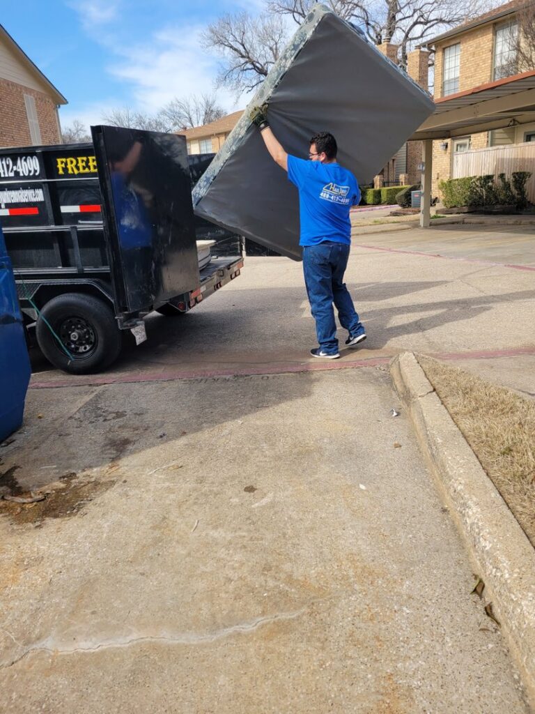 A worker from Haulaway Junk Removal Service, LLC loading a mattress onto a trailer during a junk removal job in Dallas, TX.
