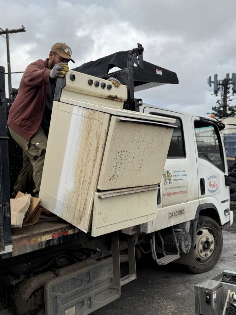 A worker from Fred's Junk Removal loading an old stove onto a junk removal truck in Chula Vista, CA.