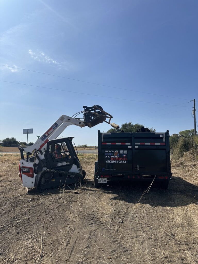 A worker loading tree branches and brush into a Big Ox Junk Removal trailer in Leander, TX, for yard waste removal.