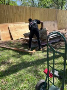 A worker from NTX Haul Away Junk Removal loading large pieces of wood and plywood debris onto a dolly in Fort Worth, TX.