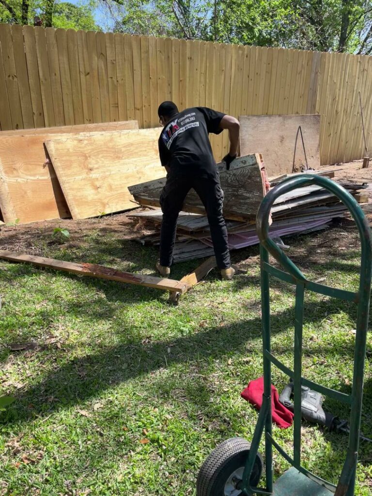 A worker from NTX Haul Away Junk Removal loading large pieces of wood and plywood debris onto a dolly in Fort Worth, TX.