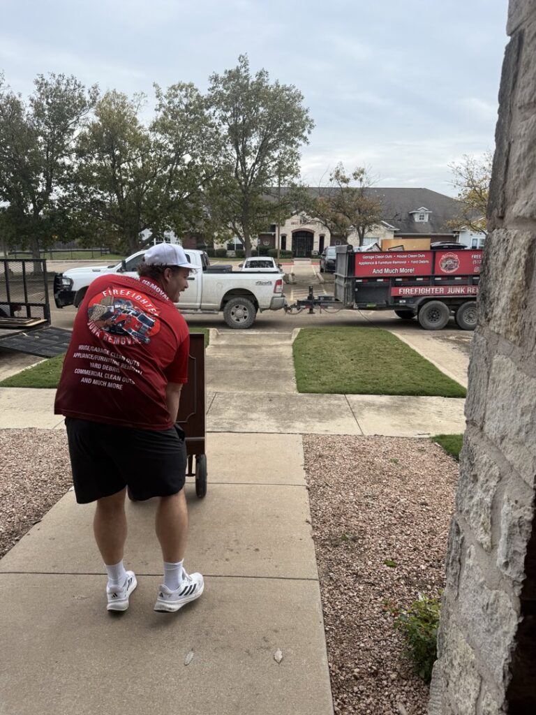 A Firefighter Junk Removal worker in Austin, TX, moving a cabinet on a dolly towards a junk removal trailer.