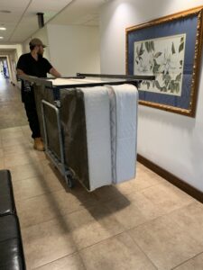 A worker from Fred's Junk Removal moving two mattresses on a dolly inside a building in Chula Vista, CA.